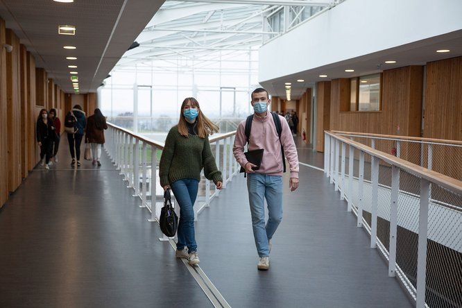 Une lycéenne et un lycéen masqués marchent dans le hall de leur lycée