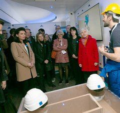 Christelle Morançais, présidente de Région avec groupe de personnes autour d'un homme en habit de chantier qui parle, dans une salle